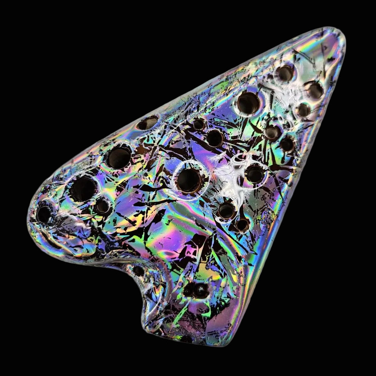 A triangular metallic pin or brooch with a holographic, iridescent finish showing purple, green, and blue reflections, decorated with multiple circular cutouts, on a textured white background.
