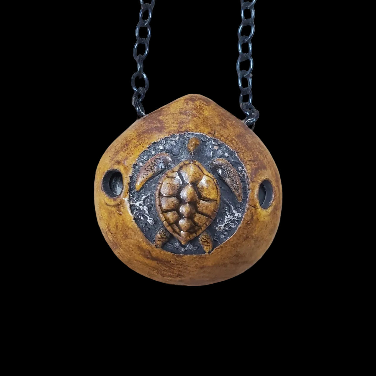 Brown pendant ocarina with turtle design on a chain against a textured beige background