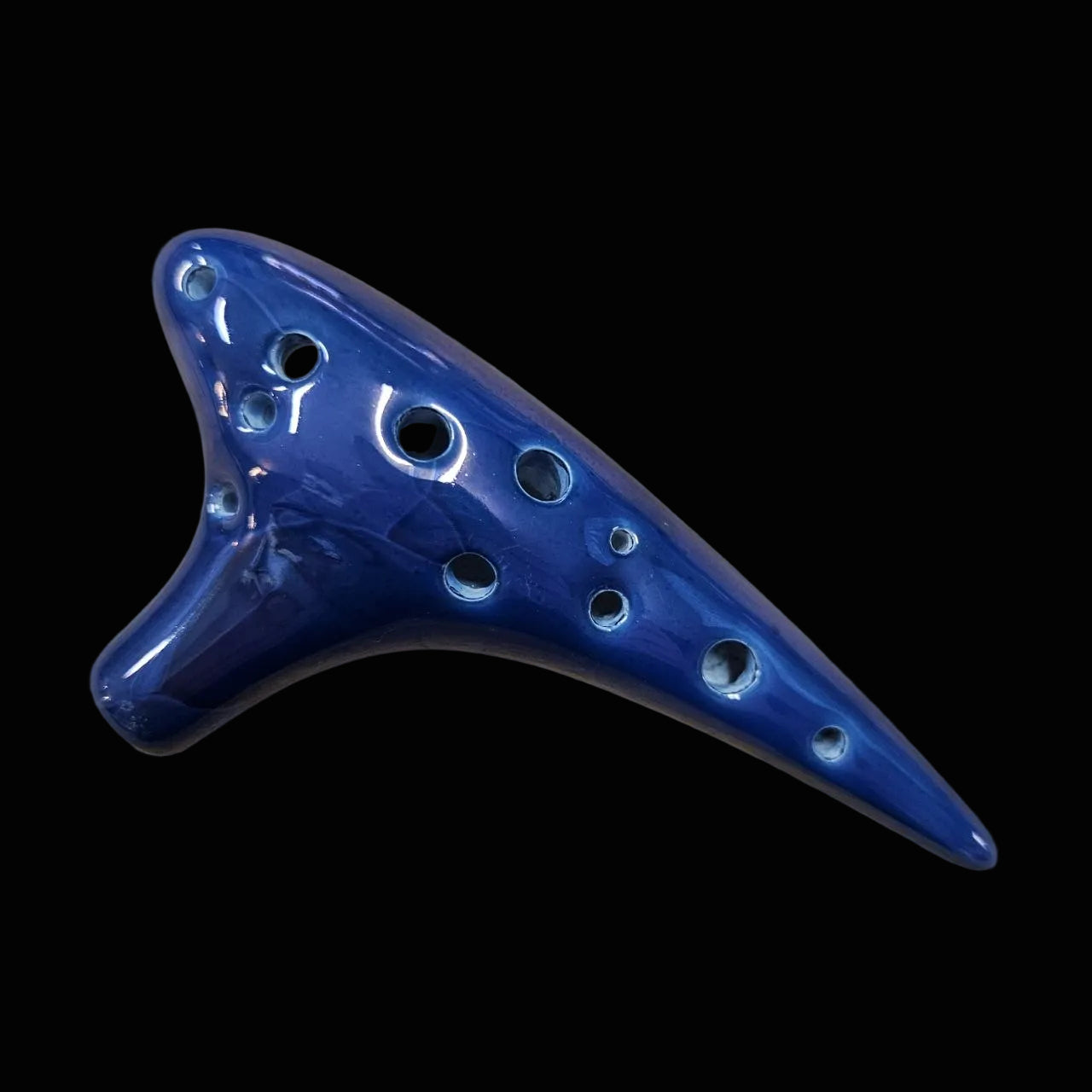 A glossy cobalt blue ceramic ocarina resting on a scratched, light brown wooden workbench.