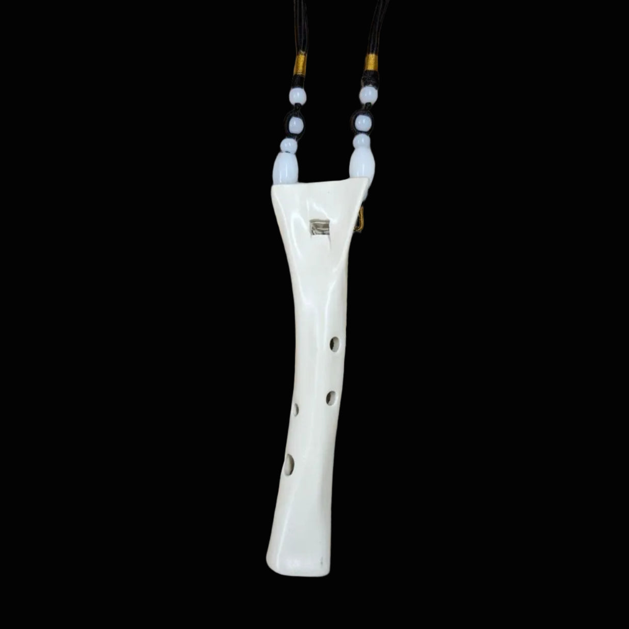 A white ceramic flute with a curved body and four finger holes, resting on a scratched wooden workbench. Black and gold neck tubes are attached to the sides.