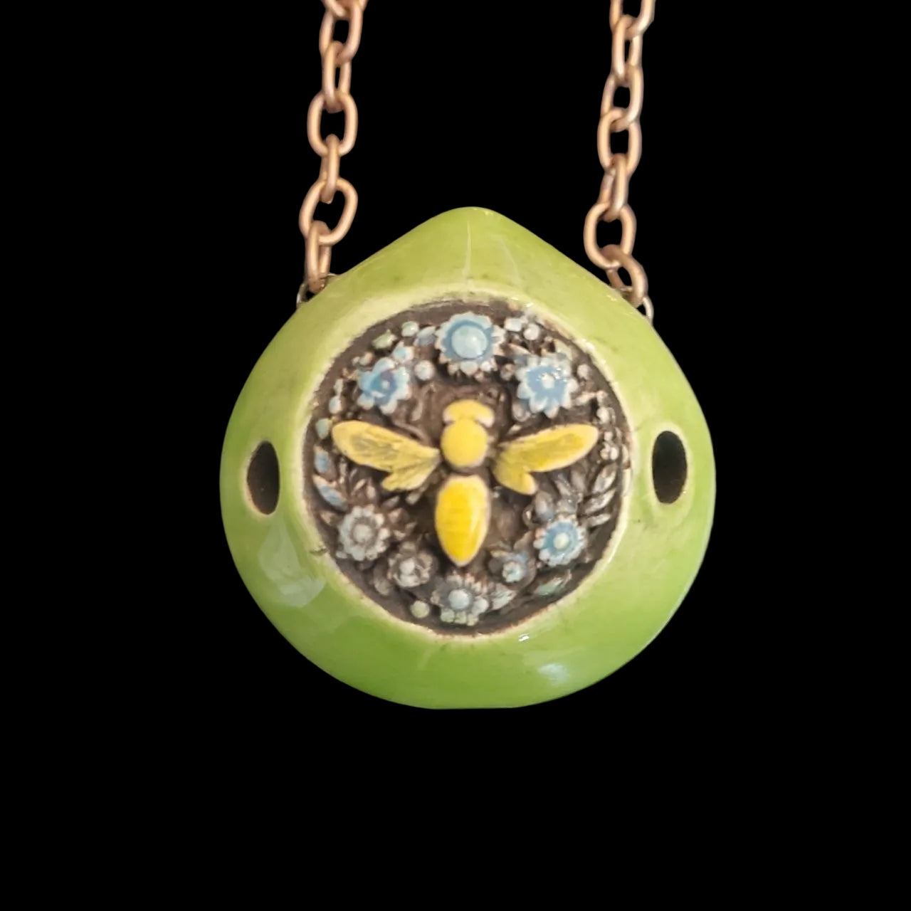 Green ceramic pendant with bee design on a chain against a dark textured background